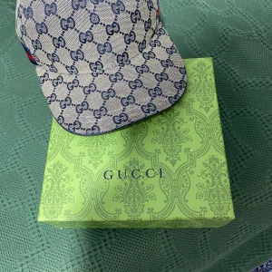 Gucci keps - Snygg keps från Gucci i beige och marinblått med klassiskt GG-monogram över hela kepsen. Kepsen har en röd och blå rand på sidan och justerbar rem baktill. Tillverkad i bomullscanvas med blått innerfoder. Perfekt för dig som vill sticka ut med lyxig streetstyle.