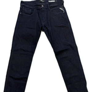 Mörkblå Replay Anbass jeans - Snygga mörkblå Replay Anbass jeans med klassisk femficksdesign och raka ben. Jeansen har en stilren look med diskreta detaljer och läderpatch bak i midjan. Perfekta för dig som gillar en tidlös och clean stil.