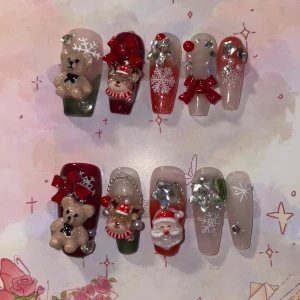 S - Juliga press-on naglar med 3D dekorationer - Set med press-on naglar i juldesign med 3D-nallar, ren, tomte, snöflingor, röda rosetter och glittriga stenar. Färgerna är rött, grönt, vitt och nude. Naglarna har glansig finish och är dekorerade med pärlor och strass för extra bling.