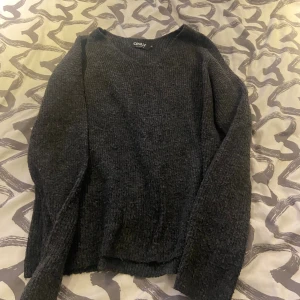 Mörkgrå stickad tröja från ONLY - Mysig mörkgrå stickad tröja från ONLY i storlek XS. Tröjan har en enkel och klassisk design med rund halsringning och långa ärmar. Perfekt för lager-på-lager och chill dagar. Snygg att matcha med jeans eller kjol.