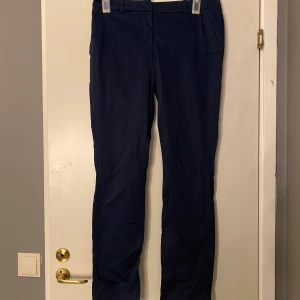 Mörkblå kostymbyxor med guldknappar - Snygga mörkblå kostymbyxor med raka ben och klassisk passform. Byxorna har bälteshällor, sidfickor och två bakfickor med guldiga knappar som detalj. Perfekta för en stilren look och tillverkade i ett mjukt bomullsmaterial.Frakt ingår inte 