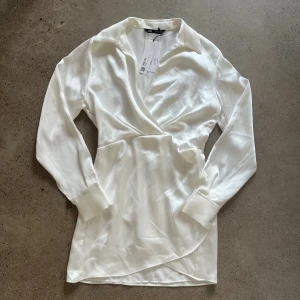 Vit klänning från Zara - Säljer en vit klänning från Zara i helt nytt skick. Klänningen är i storlek M och har en fin passform med ett skönt, glansigt material.