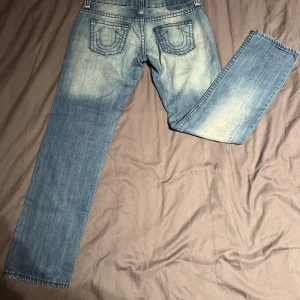 True Religion blå jeans, stl 33 - Säljer ett par klassiska blå jeans från True Religion med ikoniska bakfickor och slitna detaljer. Jeansen har raka ben och tydliga kontrastsömmar. Inte riktigt min stil längre därför ska dom säljas. 
