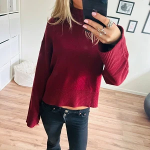 Vinröd stickad polotröja - Säljer en vinröd stickad polotröja med croppad passform och breda, ribbade muddar vid ärmslut och nederkant. Tröjan har hög krage och är perfekt för dig som gillar en chill och trendig look. Supermjuk och skön att bära under kyliga dagar.