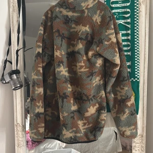Camouflage teddyjacka från 157 - Säljer en fet teddyjacka från 157 i camomönster med bruna, gröna och beige toner. Jackan har hel dragkedja, hög krage och en svart bröstficka med dragkedja. Perfekt för kalla dagar och riktigt skön att ha på sig.
