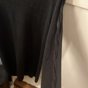 Svart stickad tröja med snörning Bodyflirt - Svart stickad tröja från Bodyflirt med coola snörningsdetaljer och hålmönster vid axlarna och längs ärmarna. Tröjan har rund hals och långärmad passform, perfekt för dig som gillar edgy och unik stil.