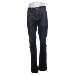 Mörkblå slimfit jeans från Nudie - Snygga mörkblå jeans från Nudie med klassisk slimfit-passform och orange kontrastsömmar. Jeansen har fem fickor, dragkedja i gylfen och Nudie-logga på bakfickan. Tillverkade i slitstarkt denim med en cool tvättad look. Dragkedjan e paj men annars nyskick