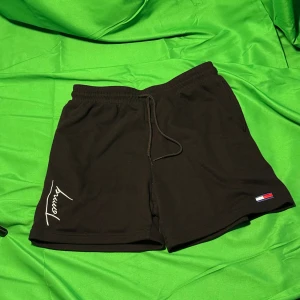 Svarta shorts från Tommy Hilfiger - Svarta shorts från Tommy Hilfiger med elastisk midja och snörning. Klassisk logga på ena benet och broderad signaturdetalj. Mjukt material som känns skönt mot huden och passar perfekt till sommaren.Liknande modell som originalet!