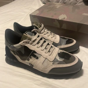 Valentino rockrunners - Snygga Valentino Garavani Rockrunner sneakers med grått och svart camouflagemönster. Skorna har detaljer i mocka och skinn, samt klassisk snörning. Sulan är svart och designen är riktigt clean och modern. Perfekta för vintern! 