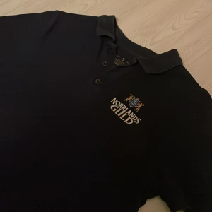 Mörkblå pikétröja Norrlands Guld - Snygg svart pikétröja från Norrlands Guld med broderad logga på bröstet. Skick 6/10 syns att den är tvättad men inget som syns när man bär den. Storlek S. Skriv vid minsta fundering!