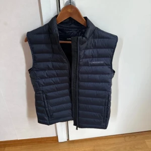 Svart dunväst från J.Lindeberg - Snygg mörkblå dunväst från J.Lindeberg med quiltad design. Knappt använd, nypris 2199kr