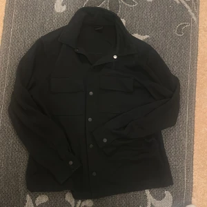Svart overshirt med knappar - Köpte den men den passade en, vill sälja den snabbt så pris kan diskuteras.
