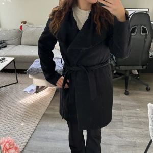 Svart kappa från Esprit med guldknappar - Stilren svart kappa från Esprit med bred krage och dekorativa guldknappar framtill. Kappan har en klassisk, längre modell och är fodrad på insidan för extra komfort. 