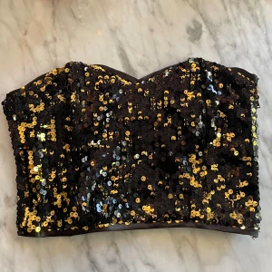Paljett tubtopp - Svart och guldig paljett topp med dragkedja på sidan. Köpte second hand passar xs/s 