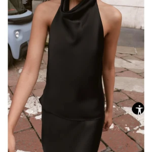 Svart halterneck topp i satin - Snygg svart halterneck topp från Zara i glansigt satinmaterial med öppen rygg och hög krage. Toppens släta yta ger en lyxig känsla och den är ärmlös med en loose passform. Perfekt för dig som vill ha en stilren och trendig look.(Endast använd en gång)🥰