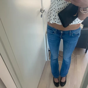 Populära Lågmidjade blå bootcut jeans - Snygga lågmidjade jeans i klassisk blå tvätt med bootcut-snitt. Jeansen har fem fickor, dragkedja och knapp framtill. Perfekta för dig som gillar en avslappnad men ändå trendig look. Materialet är mjukt och följsamt jeans.