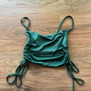 Grön festtopp  - Snygg grön linnetopp med smala axelband och croppad passform. Toppen har snörning på båda sidorna som ger en cool och justerbar look. Perfekt för dig som gillar trendiga och enkla plagg med lite edge.