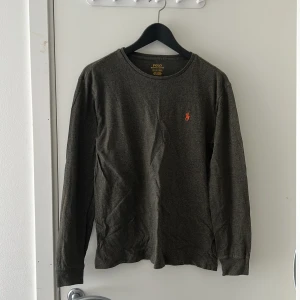  Polo Ralph Lauren tröja - Mörkgrå långärmad tröja från Polo Ralph Lauren med klassisk rund hals och orange broderad logga på bröstet. Tillverkad i mjuk bomull, perfekt för höst och vinter ❄️ Slim fit storlek S😆