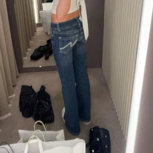 Blå bootcut jeans från Nelly  - Säljer ett par blå jeans med bootcut passform och snygga kontrastsömmar på bakfickorna. Jeansen har låg midja och klassisk femficksdesign. Perfekta för dig som gillar en avslappnad men trendig stil. I storlek 34