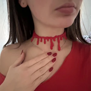 Röd choker med droppformad design - Cool röd choker som ser ut som droppande blod, perfekt för att sticka ut. Halsbandet har en unik och edgy look med oregelbundna droppar runt hela bandet. Kedja i silverfärg för justerbar passform. Grym accessoar för dig som gillar alternativ stil.