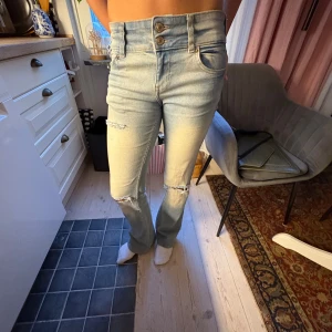 Ljusblå bootcut jeans med knappar - Snygga ljusblå jeans med bootcut passform och medelhög midja. Jeansen har slitna detaljer vid knäna och dubbla knappar framtill. Klassisk femficksmodell och stretchigt denimtyg som sitter skönt. Perfekt för dig som gillar en avslappnad men trendig look. 😻💖Jeansen går även att vika ner så att dom blir low waist!!!