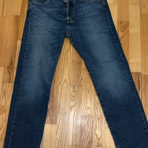Levi's 501 jeans blå W31 L30 - Klassiska Levi's 501 jeans i blå denim med raka ben och normal passform. Byxorna har fem fickor, knappgylf och den ikoniska läderpatchen bak i midjan. Perfekt för dig som gillar tidlös stil och vill ha ett par schyssta jeans.