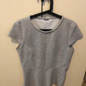 Ljusgrå kortärmad topp - En stilren ljusgrå topp med rund halsringning och korta ärmar. Toppen har en lätt figursydd passform och är tillverkad i ett mjukt, stretchigt material som känns bekvämt mot huden. Perfekt att matcha med jeans eller kjol för en enkel och snygg look.