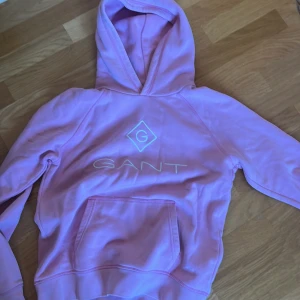 Rosa hoodie från GANT med logga - Säljer en rosa hoodie från GANT med broderad logga framtill. Tröjan har huva, magficka och långa ärmar. Tillverkad i mjuk bomull, perfekt för en chill och avslappnad stil.