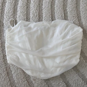 Vit bandeau tubtopp från Cider - Säljer en snygg vit bandeau tubtopp från Cider med draperad mesh och dragkedja i ryggen. Toppen är axelbandslös och har en stilren look som passar perfekt till sommarens outfits.