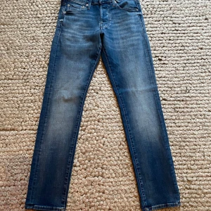 Blå Slim Glenn jeans storlek 27/30 - Snygga blå jeans från Slim Glenn i storlek 27/30. Modellen har en slim passform med klassisk femficksdesign och lätt tvättade detaljer. Perfekta för dig som gillar en smal siluett och stilren look. Materialet är mjukt och följsamt jeans.