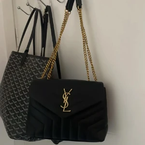 Svart axelväska från Saint Laurent - Säljer en svart axelväska från Saint Laurent med guldfärgade kedjor och YSL-logga framtill. Väskan är quiltad och har dragkedja på insidan. Perfekt för dig som vill ha en lyxig accessoar med klassisk design. Den är ej äkta❤️