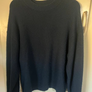 Mörkblå stickad tröja från H&M - En enkel och stilren mörkblå stickad tröja från H&M. Tröjan har rund halsringning och långa ärmar, perfekt för lager-på-lager under kyliga dagar. Den är väl använd men har inga defekter förutom att den är lite nopprig