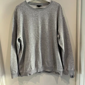 Grå sweatshirt från H&M Relaxed Fit - En stilren grå sweatshirt från H&M i relaxed fit. Tröjan har rund halsringning, långa ärmar och ribbade muddar vid ärmslut och nederkant. 