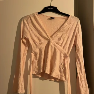 Ljusrosa knyttopp från Gina Tricot - Säljer en ljusrosa knyttopp från Gina Tricot i storlek XXS. Toppen har lång ärm, v-ringning och knytband i midjan. De funkar även i xs 