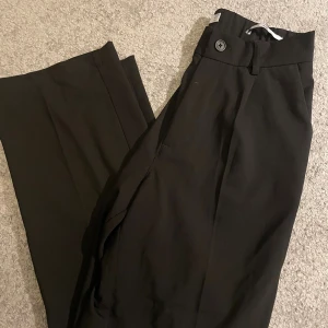 Svarta wide kostymbyxor från Bershka (stora i storlek) - Svarta kostymbyxor från Bershka i storlek XS. Byxorna har en wide fit, hög midja och stängs med knapp och dragkedja. Snyggt skräddad look med raka, vida ben och diskreta fickor framtill. Perfekta för en clean och stilren outfit. (Byxorna är lite större i storleken så att dem passar upp till storlek M)