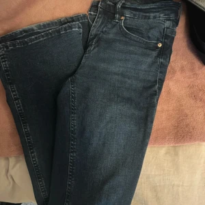Mörkblå jeans från Weekday, strl 32 - Säljer ett par mörkblå jeans från Gina Tricot i klassisk femficksmodell. Jeansen har utsvängda ben, normal passform och är tillverkade i mjukt denimtyg. Snygga detaljer med kopparfärgade nitar och dragkedja i gylfen.