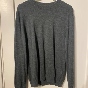 Grå merinotröja från These Glory Days - Snygg mörkgrå stickad tröja från These Glory Days i mjuk och exklusiv merinoull. Klassisk rund hals och långärmad modell med ribbade muddar vid hals, ärmslut och nederkant. 