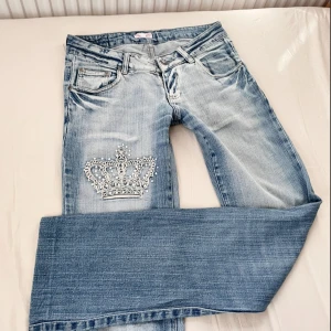 Lågmidjade crazy age liknande jeans med kronor - Ljusblåa jeans som likar crazy age med kronor på bakfickorna och högra benet, finns några pyttesmå fläck vid högra knät (bild 5) // strl M 💗 // midja 38cm tvärsöver, innerbenslängd 82cm