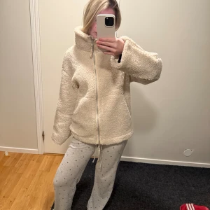 Beige teddyjacka med dragkedja - Mysig beige teddyjacka med hög krage och hel dragkedja framtill. Jackan har en loose passform och är tillverkad i fluffigt fleece-material som håller dig varm. Perfekt för kyliga dagar och enkel att styla till olika outfits. Missfärrgad på insidan längst ner men inget som syns när man har på sig den 