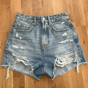 Jeansshorts Stradivarius - Säljer ett par ljusblå högmidjade jeansshorts från Stradivarius med råa kanter och slitna detaljer framtill och baktill. Perfekta för sommardagar när du vill ha en edgy look.