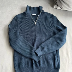 Marinblå stickad half zip-tröja - Säljer en marinblå stickad tröja från Zara med ribbad struktur och half zip-dragkedja i halsen. Tröjan har lång ärm och hög krage, perfekt för lager-på-lager under kyliga dagar.