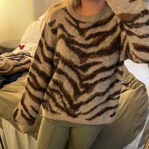 Beige zebramönstrad stickad tröja - Supermysig stickad tröja i beige med brunt zebramönster. Tröjan har rund halsringning, lång ärm och en loose fit som ger en chill vibe. Den är jätte skön och luftig.  Tröjan är i storlek L men sitter som på bilderna och är absolut inte för stor utan mer lös. 