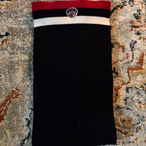 Moncler halsduk  - Säljer en fet Mörkblå halsduk från Moncler med klassiska röda och vita ränder i ena änden samt Moncler-logga. Halsduken är rektangulär och stickad. Halsduken har inga defekter eller syn på användning. Jag kan gå med på någon rimlig prutning.