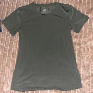 Mörkgrön sport t-shirt från H&M - Snygg mörkgrön t-shirt från H&M Sport i storlek 146/152. Modellen är klassisk med rund hals och korta ärmar, perfekt för träning eller chill. Materialet är mjukt och lätt polyester som andas bra. Enkel och stilren design utan mönster eller detaljer.