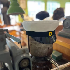 Klassisk Studentmössa 52-63 - Klassisk studentmössa med vit ovandel i tyg, svart band och blank svart skärm. Framtill sitter en gul och blå kokard. Insidan har ett foder i gult och blått. Perfekt för studenten och högtider.