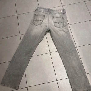 Replay ljusgrå jeans straight fit - Säljer ett par ljusgrå jeans från Replay med klassisk femficksdesign och raka ben. Jeansen har subtila slitningar och en snygg tvättad look. Tillverkade i mjuk bomullsdenim med Replay-logga på bakfickan. Perfekta för dig som gillar stilrena och bekväma jeans.stolek H:158 dom har en liten vi fläck på sig men ingen man tänker på när dom e på.