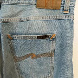 Ljusblå jeans från Nudie Jeans, steady eddie - ljusblå jeans från Nudie Jeans. Jeansen har broderad bakficka och normal passform. Tillverkade i bomull och perfekta för en avslappnad stil. Modell steady eddie och har en straight passform storlek 32/32 men uppklippt någon centimeter på benet. Liten fläck på ena låret som jag inte försökt få bort men märks knappast