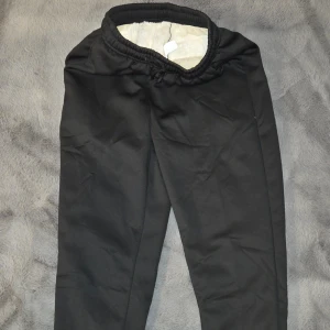 Svarta fleecefodrade mjukisbyxor, S - Mysiga svarta mjukisbyxor med vitt fleecefoder på insidan. Byxorna har resår och snörning i midjan samt muddar vid bensluten. Perfekta för kalla dagar när du vill vara extra bekväm.