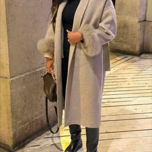 Beige kappa med pälsdetaljer storlek s - Snygg beige kappa med fluffiga pälsdetaljer vid ärmsluten och knytbälte i midjan. Modellen är lång och har en loose passform med bred krage. Perfekt för dig som vill ha en stilren och lyxig look under höst och vinter.