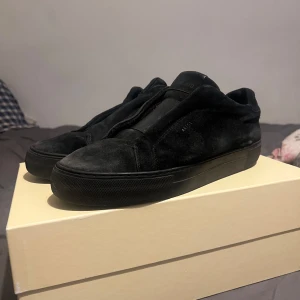 Svarta sneakers från Arigato i mocka - Svarta sneakers från Axel Arigato, modell Clean 360 Laceless. Skorna är i mjuk mocka med elastisk panel framtill istället för snörning. Snygg minimalistisk design med platt sula och diskret logga på sidan. Perfekta för dig som gillar stilrena och bekväma skor.